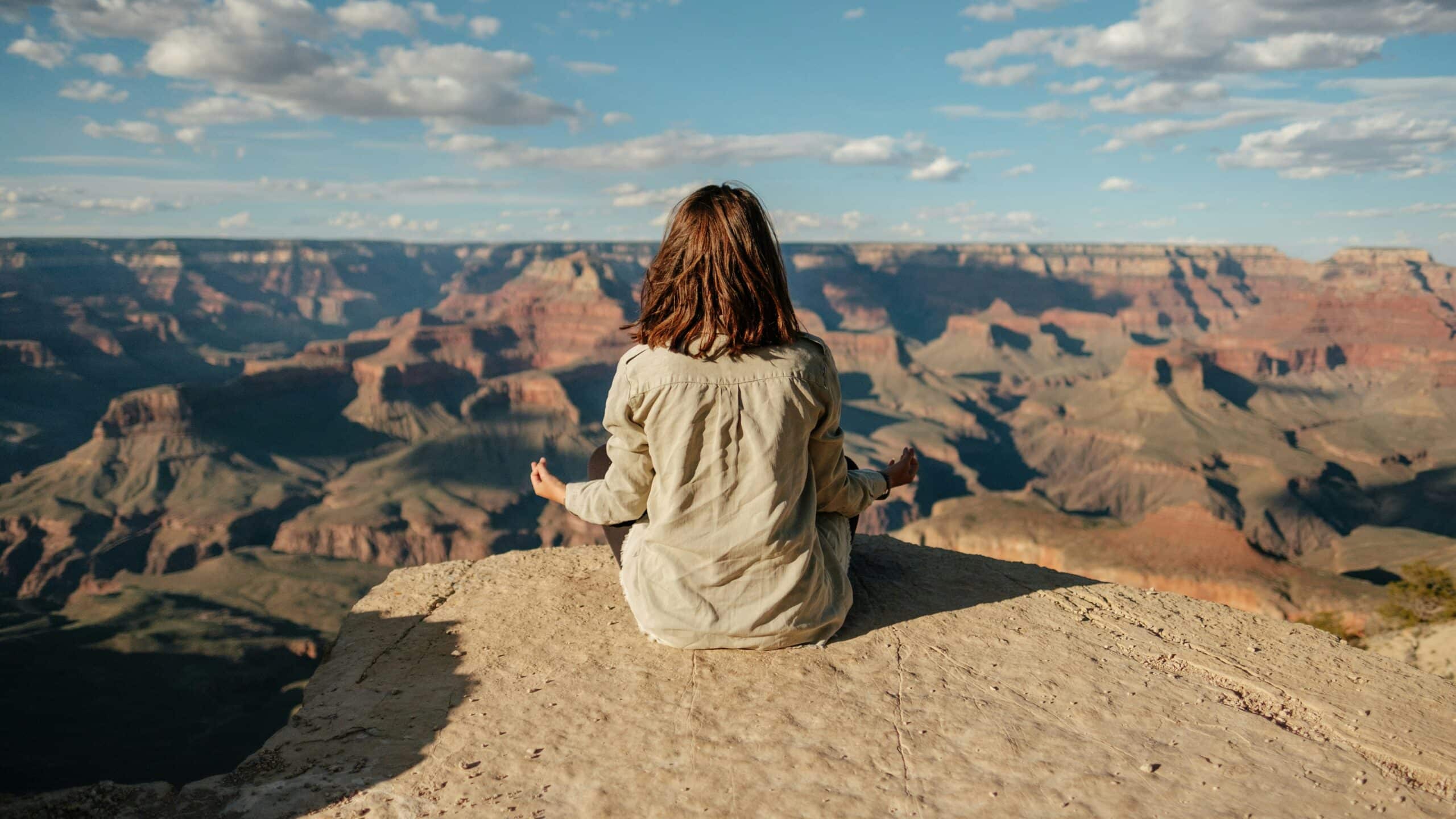 Personne méditant face à un canyon pour illustrer le coaching en gestion du stress, la gestion de la charge mentale et la recherche d’équilibre chez les actifs.