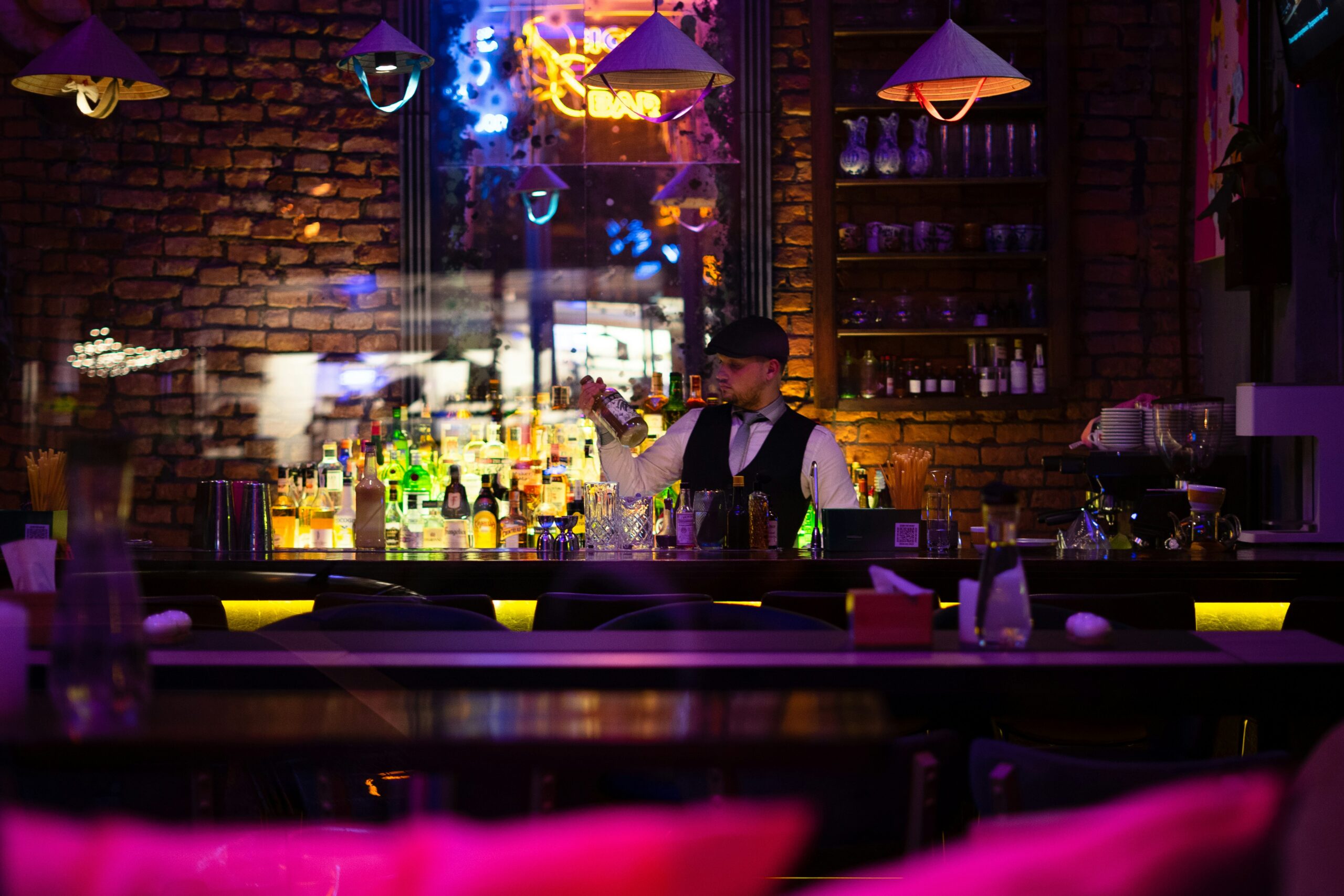 Bartender préparant un cocktail dans un bar Cannes à l'ambiance élégante, avec éclairages colorés, spiritueux premium et décoration chaleureuse.